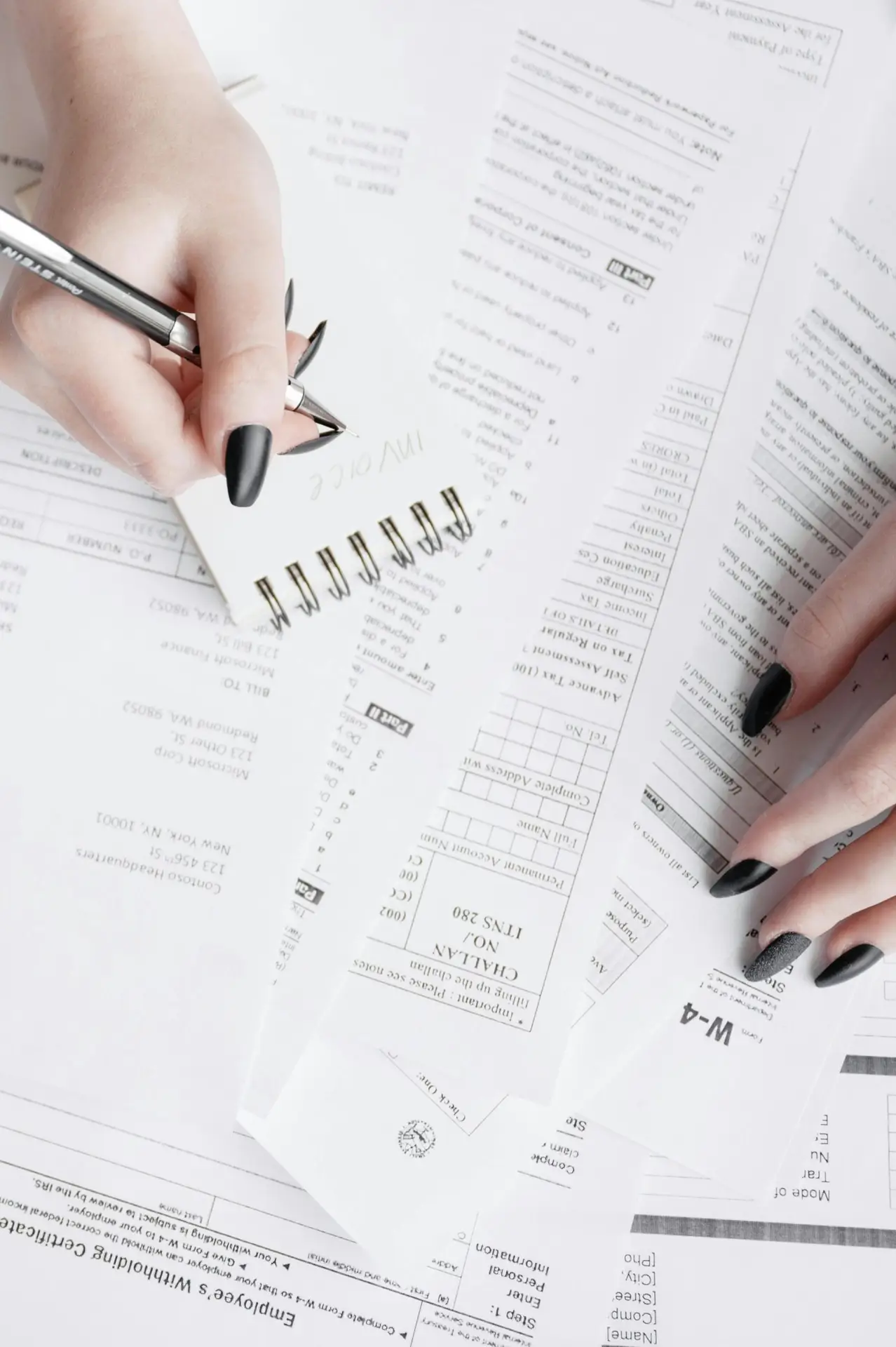 Close-up of hands writing notes on a notepad over tax forms, showcasing financial planning.